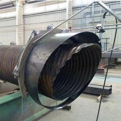 A large metal pipe with a damaged, crumpled end is held in place by a metal frame in an industrial setting. The pipe appears to have been forcibly crushed or bent inward.