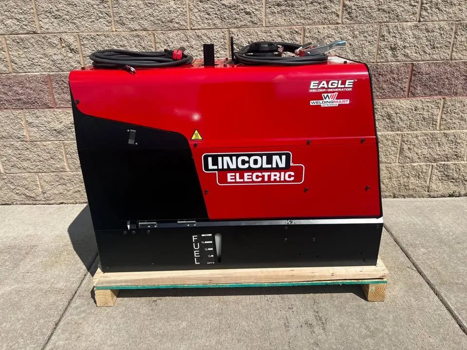 A Lincoln Eagle 10,000 Plus Engine Drive Factory Demo Welder (U2343-4), red and black, sits on a wooden pallet outside against a beige brick wall with coiled cables on top and the FUEL gauge visible.