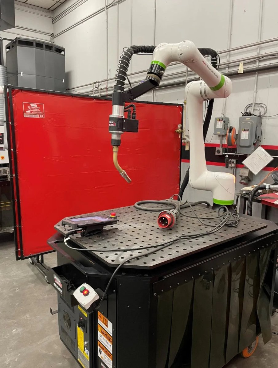 Lincoln Cooper CRX-10iA/L Aluminum Welding Cobot Cart on metal worktable, tools, and red safety screen in industrial workshop.