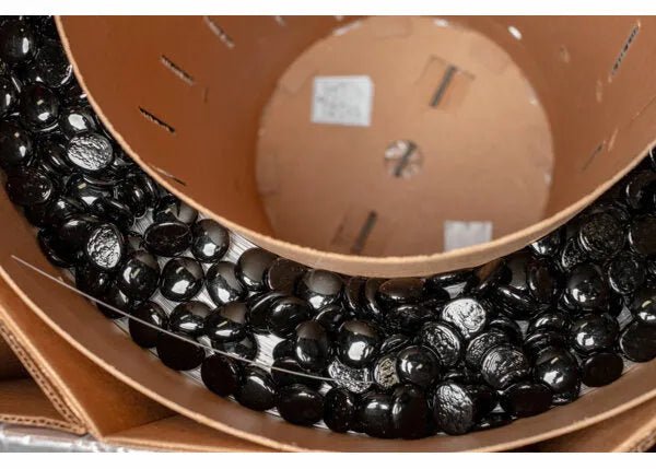 A close-up view of a large cardboard spool filled with shiny black glass stones, packed tightly within the circular container, resembling how MIG welding wire like SuperGlaze 5356 is wound for industrial use.