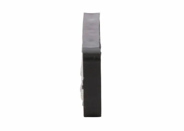 A flat, rectangular, dark object—probably a Harris Model 26-L Ignitor Renewal Flint (9004484)—stands upright on its narrow edge against a white background, with its thin side facing the camera.