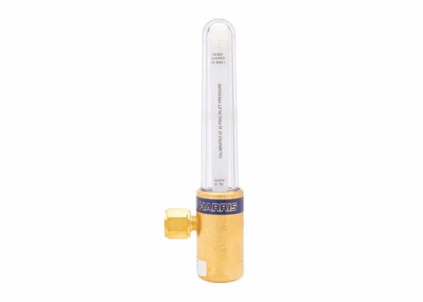 A brass flashback arrestor with a clear cylindrical tube, labeled Harris, used for gas-shielded welding safety. The device features a hexagonal connector on one side and integrates SCFH flow control for precise gas regulation.