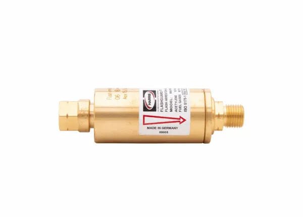 A brass cylindrical flashback arrestor with threaded connectors on both ends, a label showing specifications for fuel gas, and a red arrow indicating flow direction.