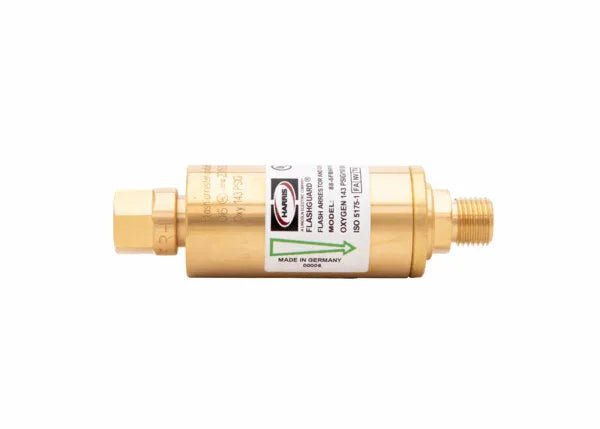 A brass cylindrical flashback arrestor with threaded ends and a label indicating manufacturing details, including Made in Germany, an arrow for flow direction, and technical specifications.