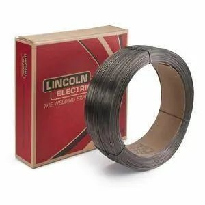 A coil of Lincoln .052 METALSHIELD MC-6 welding wire, 60lbs. (ED030550), sits before a red and tan Lincoln Electric box with the logo and “The Welding Experts” in white text. The metal-cored wire has an empty cardboard core.