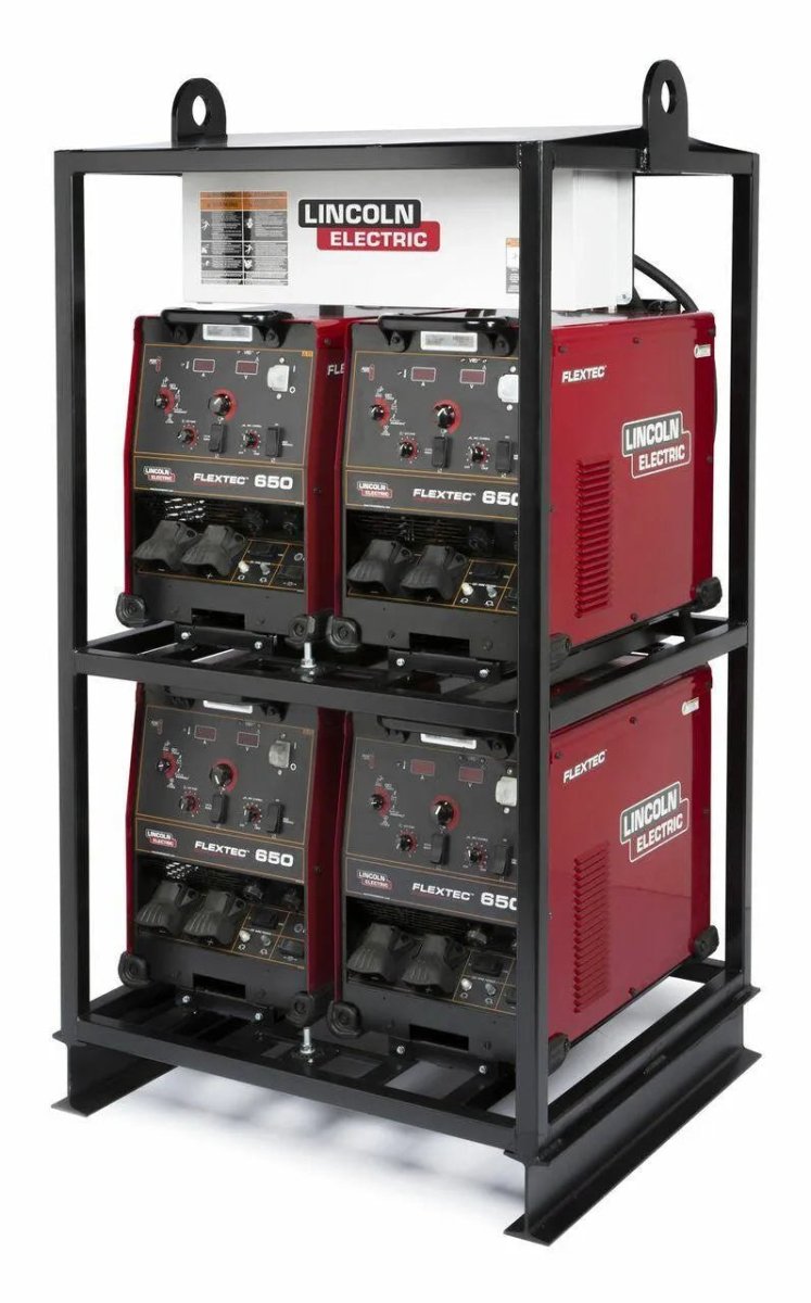 Four red Lincoln Electric Flextec 650 welding machines are stacked in two rows within a black metal rack, creating a robust multi-operator welder system. The equipment features various control knobs and connection ports on the front panels.