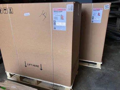 Lincoln Power MIG 360MP welder in cardboard boxes on pallets, warehouse floor—WeldingMart welding equipment storage.