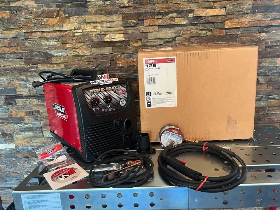 Lincoln Work Pack 125 U2699-3 welding kit on table with cables, clamp, wire spool, and box, ideal for flux-cored projects.