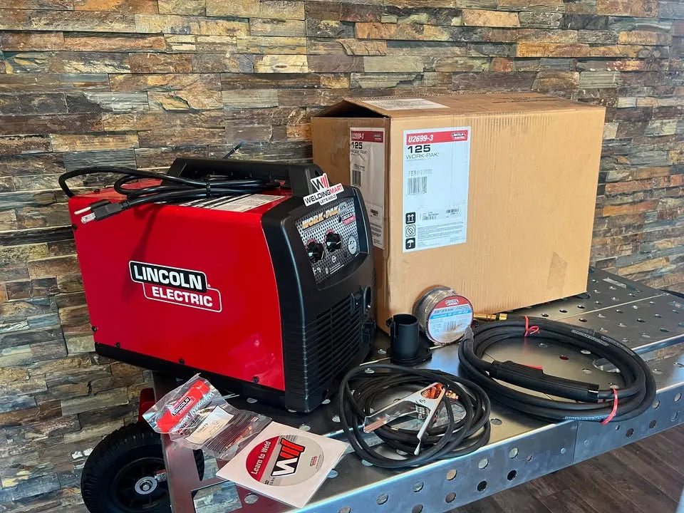 Lincoln Work Pack 125 U2699-3 with welding cables, wire spool, and manuals on workbench—WeldingMart flux-cored welder kit.
