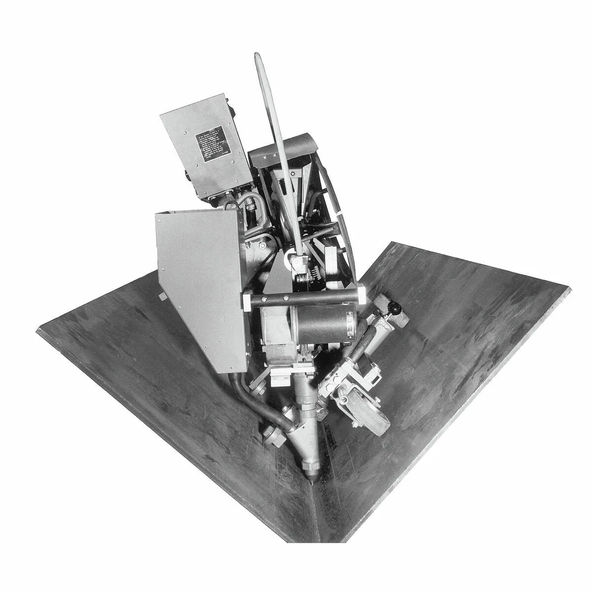 Black and white image of the Lincoln Flat Fillet Adapter Kit K229, featuring metal panels, guide wheels, and components within a large V-shaped structure. Wires, pipes, and a cylinder indicate its industrial or scientific function on a plain white background.