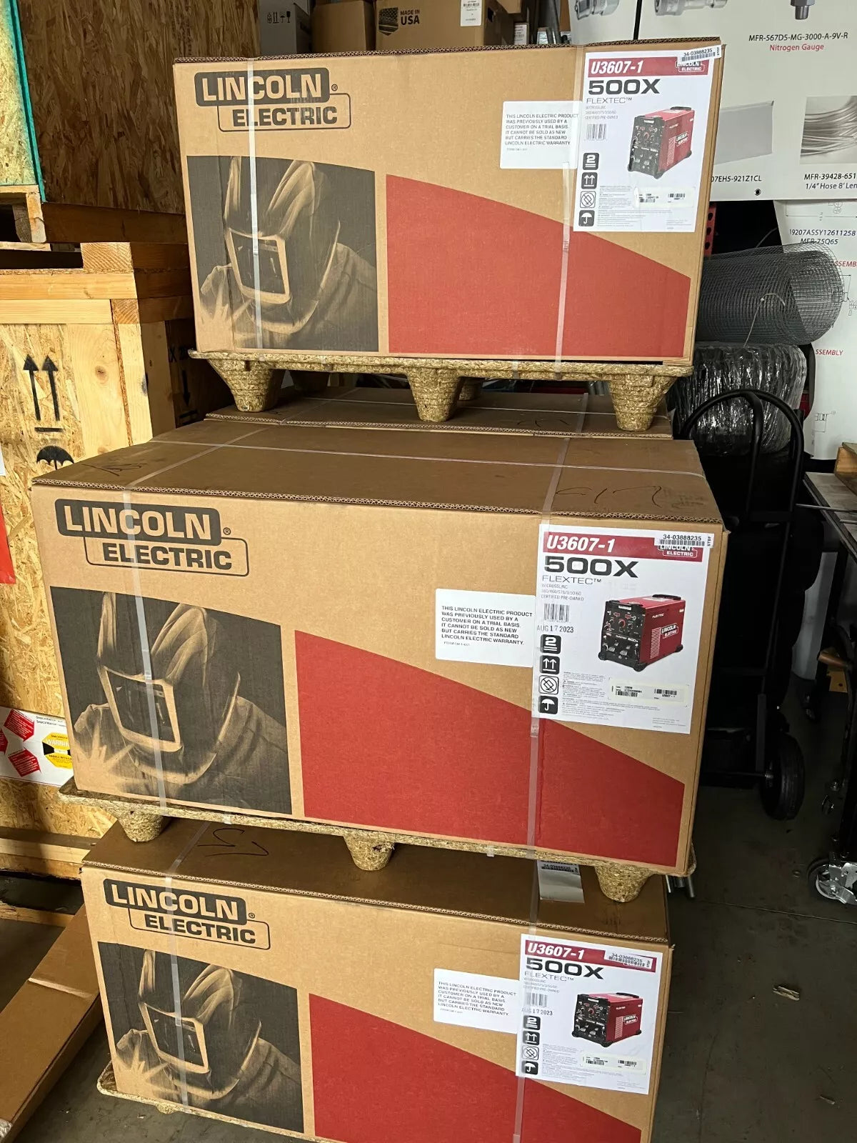 Lincoln Flextec 500X Multi-Process Welders (U3607-1) stacked on pallet in warehouse with welding equipment and storage crates.