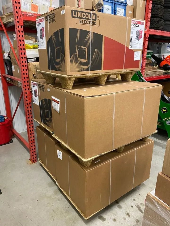 Lincoln Flextec 500X Demo Welder on pallets in WeldingMart warehouse with welding tools, boxes, and equipment on shelves.