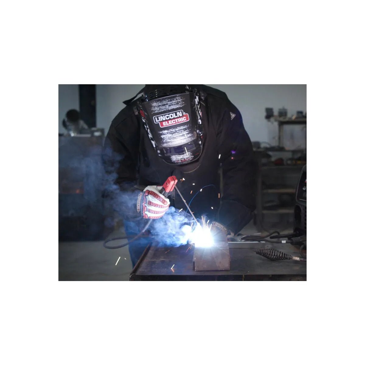 Welder using Lincoln Invertec V155-S Stick Welder K2605-1 with PPE, metalwork sparks, smoke in WeldingMart industrial workshop.