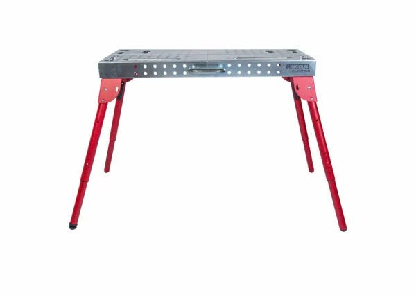 The Lincoln Portable Welding Table and Workbench K5334-1 has a rectangular silver tabletop with holes and slots, four red angled adjustable legs for stability, and a side handle for carrying. The bench is shown against a plain white background.