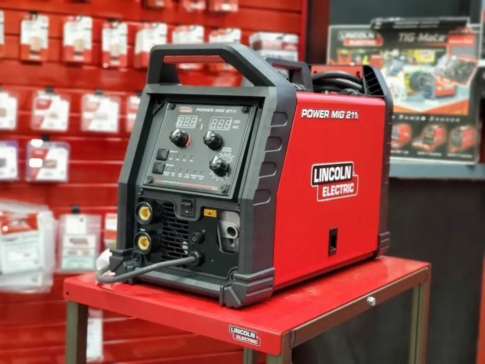 Lincoln Power MIG 211i MIG Factory Demo Welder U6080-1 on red table with welding accessories at WeldingMart, red wall background.