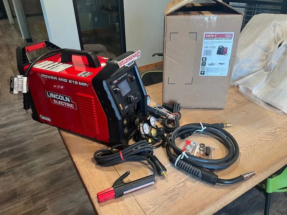 Lincoln Power MIG 215 MPi Welder with cables, welding torch, and accessories on table near box—WeldingMart welding equipment.