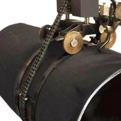 A welding machine with wheels and a chain is attached to a large black pipe, preparing for automated welding or cutting along the pipes seam.