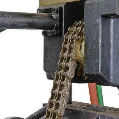 A machine extruding a continuous, metallic roller chain, with the chain emerging from a mold or press against a white background.