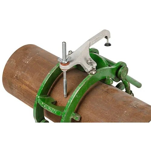 A green pipe clamp with a silver alignment tool attached is secured around a large brown metal pipe, positioning a rod perpendicular for precise pipe alignment.