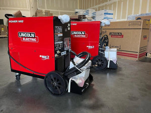 Lincoln Power MIG 256 Welders (U3068-1) with hoses on wheels at WeldingMart warehouse, surrounded by boxes and welding supplies.