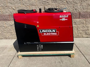 A Lincoln Eagle 10,000 Plus Engine Drive Factory Demo Welder (U2343-4), red and black, sits on a wooden pallet outside against a beige brick wall with coiled cables on top and the FUEL gauge visible.