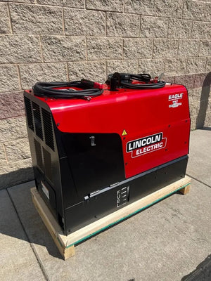 A Lincoln Eagle 10,000 Plus Engine Drive Factory Demo Welder (U2343-4) in red and black rests on a wooden pallet outside by a tan brick wall on a concrete sidewalk, cables coiled on top.