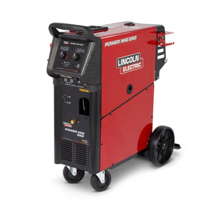 A red and black Lincoln Electric Power MIG 262 welding machine on two wheels with a handle, control knobs, display panel, and power switches visible on the front. The unit has a sturdy metal build and side vents for cooling.