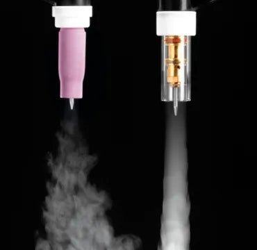 Two different nozzles, used with a TIG torch, expel mist or vapor downward against a black background. The left nozzle emits a wider, soft mist like a Large Diameter Gas Saver, while the right nozzle releases a narrow, concentrated spray.