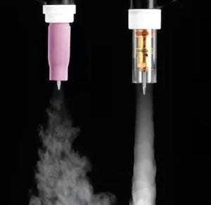 Two different nozzles, used with a TIG torch, expel mist or vapor downward against a black background. The left nozzle emits a wider, soft mist like a Large Diameter Gas Saver, while the right nozzle releases a narrow, concentrated spray.