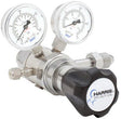 A close-up of the Harris Regulator 722C-250-580-E shows two pressure gauges (psi/kPa), a large black-and-white branded adjustment knob, and multiple metal fittings on its shiny metal body.