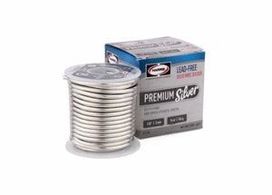 A spool of Harris 331756 Premium Silver Lead-Free Solid Wire Solder (0.118 in/3.0 mm, 25 lb box) sits in front of its blue, white, and gray packaging marked "Premium Silver" and "Lead-Free Solder Wire Solder.