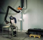 Welder using a grinder at a steel table with KEMPER 10 FT. exhaust arm; welding equipment and accessories visible nearby.