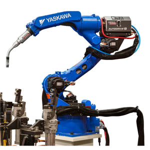 A blue Yaskawa MotoMan 2010A robotic arm with welding torch and touch-retract start is positioned over a workbench, cables wrapped around it. The Lincoln AutoDrive S Wire Feeder Air-Blast One-Pak is mounted on top. The background is plain.