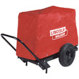 A Lincoln Electric CanVAS™ Cover (Large) K886-1 in bright red, featuring the white Lincoln Welders logo, protects the welding machine on a black metal cart with large wheels and a handle for easy transport.