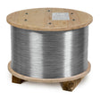 A large wooden spool holding a thick coil of shiny, silver-colored MIG welding wire, resting on a simple wooden base.