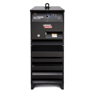 The Lincoln Idealarc AC1200 Subarc Welder - K3140-2, a tall black unit with front control knobs, switches, and ventilation slots, stands upright on the floor against a white background. Its designed for use with automatic wire feeder systems.