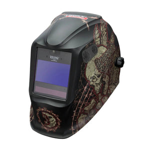 The Lincoln VIKING 2450 ADV Series Graveyard Shift Welding Helmet - K3099-5 is a black auto-darkening helmet with a large rectangular viewing window, featuring skull and feather graphics in red, beige, and brown with web patterns. Viking branding is above the lens.