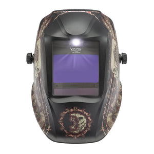The Lincoln VIKING 2450 ADV Series Graveyard Shift Welding Helmet (K3099-5) features black skull artwork, rune-like symbols, a purple-tinted auto-darkening window with 4C Lens Technology, dual adjustment knobs, and a central LED above the window.