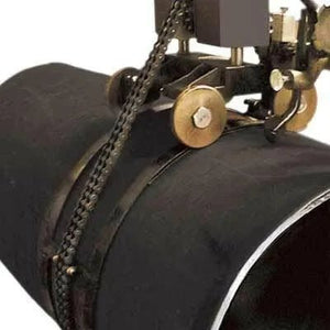 A welding machine with brass wheels and a chain is mounted on a large black metal pipe, preparing to weld the pipe seam.