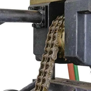 Close-up of a metal roller chain engaged with a sprocket, part of a mechanical machine with black and metallic components and some colored cables in the background.